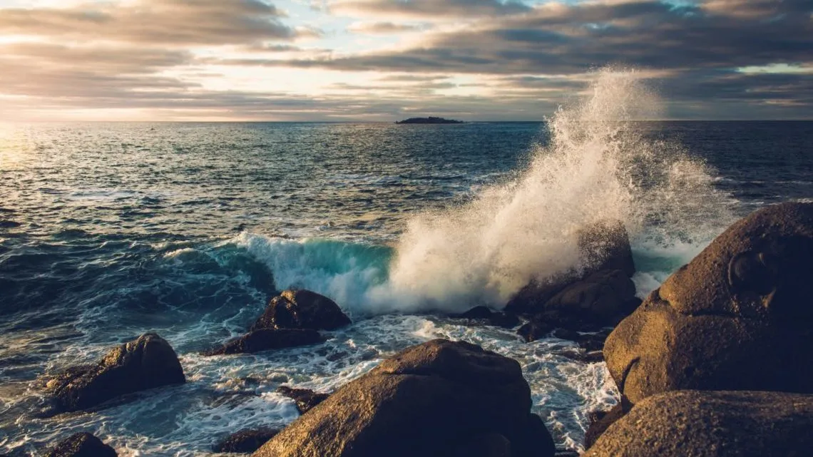 Schäumende Welle bricht sich an Felsen im Meer unter bewölktem Himmel