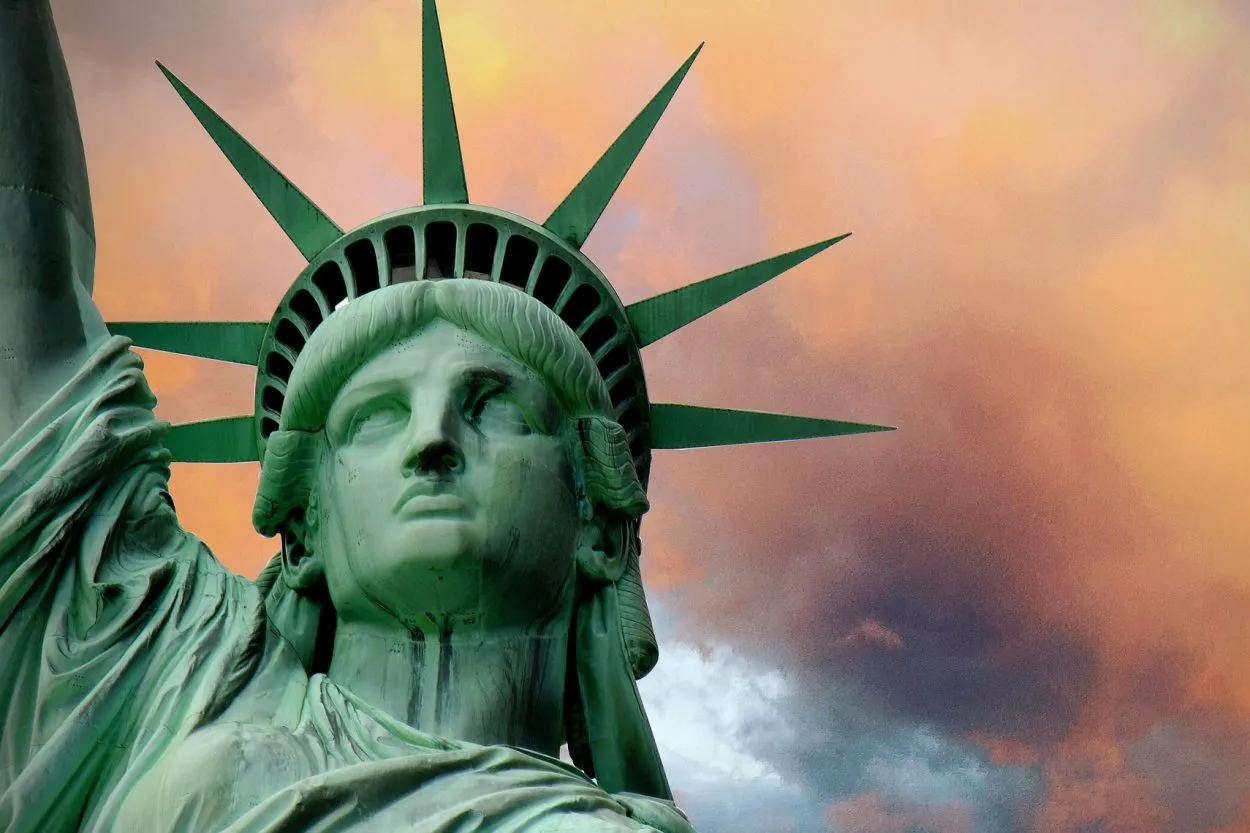 Nahaufnahme des Kopfes der Freiheitsstatue vor dramatischem orange-rotem Wolkenhimmel