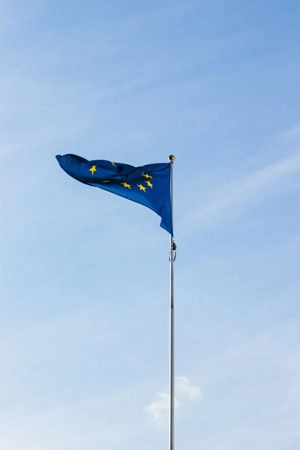 Die EU-Flagge mit gelben Sternen weht an einem Mast vor blauem Himmel.