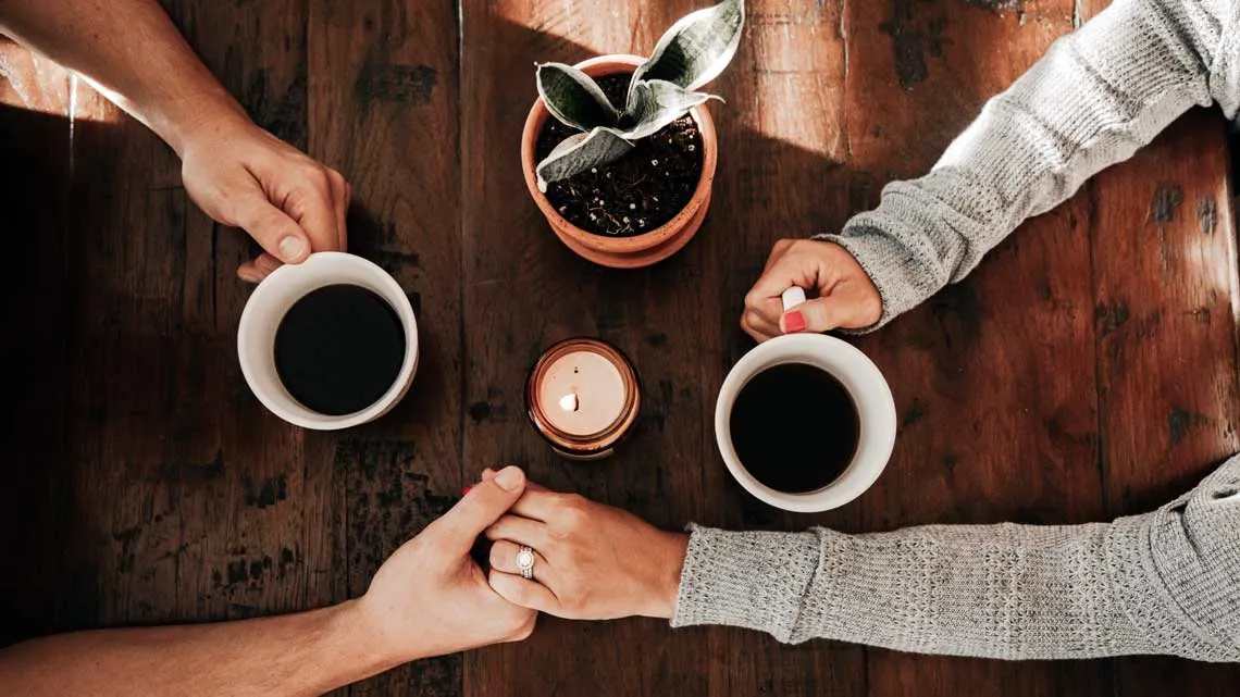 Paar hält Hände über einem Tisch mit zwei Kaffeetassen und einer Kerze