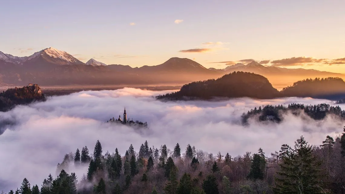 Nebelverhangenes Bergtal mit Kirchturm auf kleiner Insel bei Sonnenuntergang