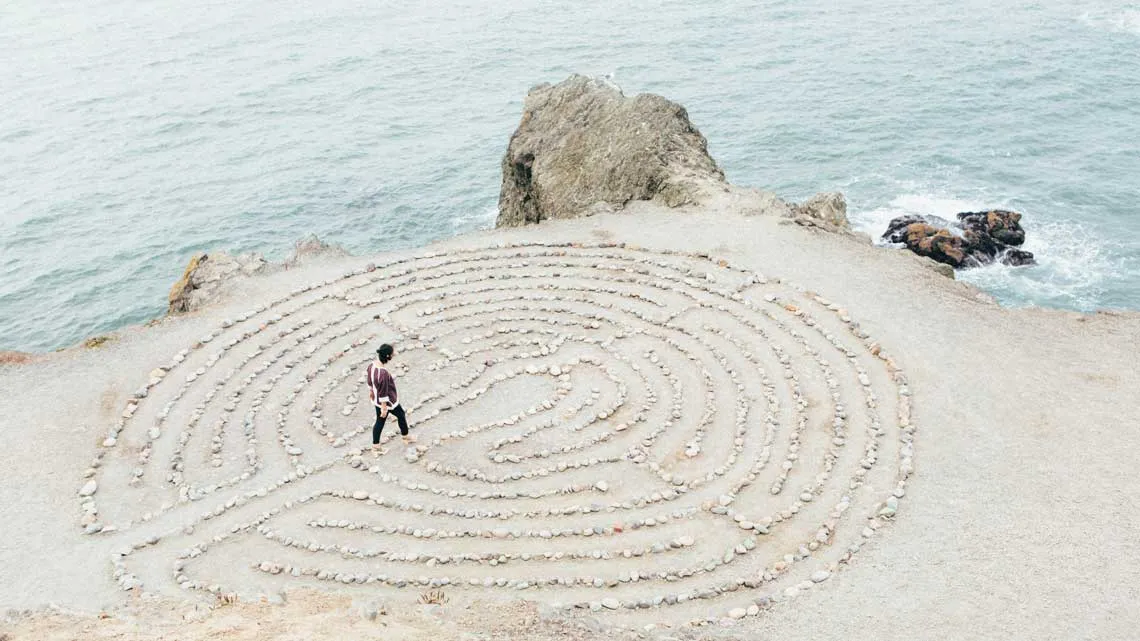 Luftaufnahme einer Person, die ein Steinlabyrinth an der Felsküste durchquert