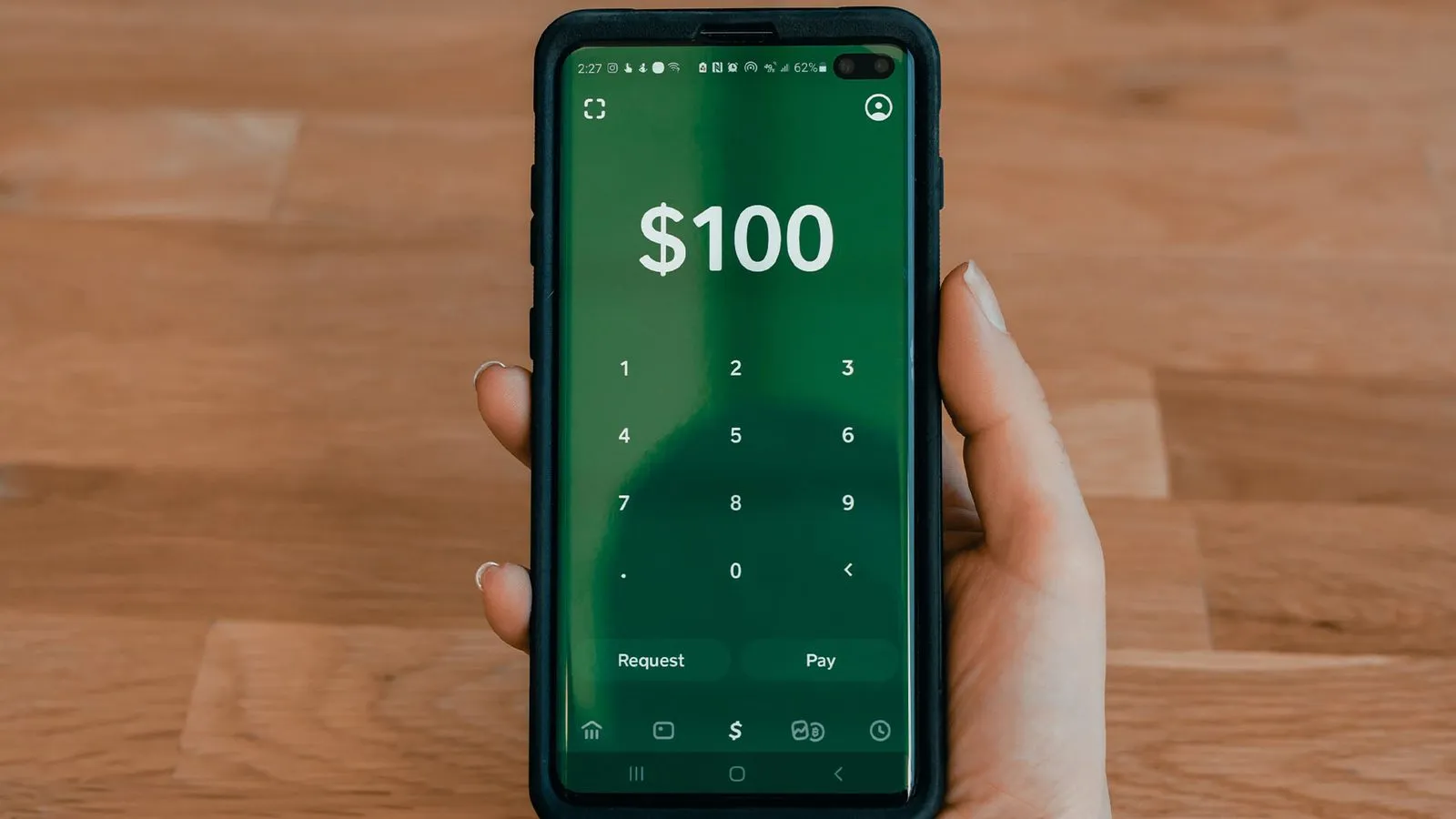 Smartphone in der Hand zeigt eine Zahlungs-App mit dem Betrag 100 US-Dollar und Zifferntastatur