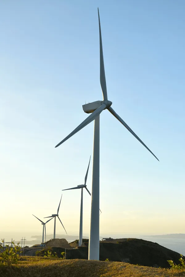 Windräder auf einer Küstenanhöhe vor Meer und Himmel im Abendlicht.