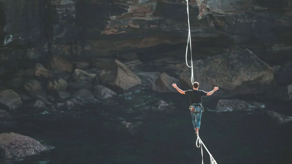 Person balanciert mit ausgebreiteten Armen auf einer Slackline über einer Schlucht