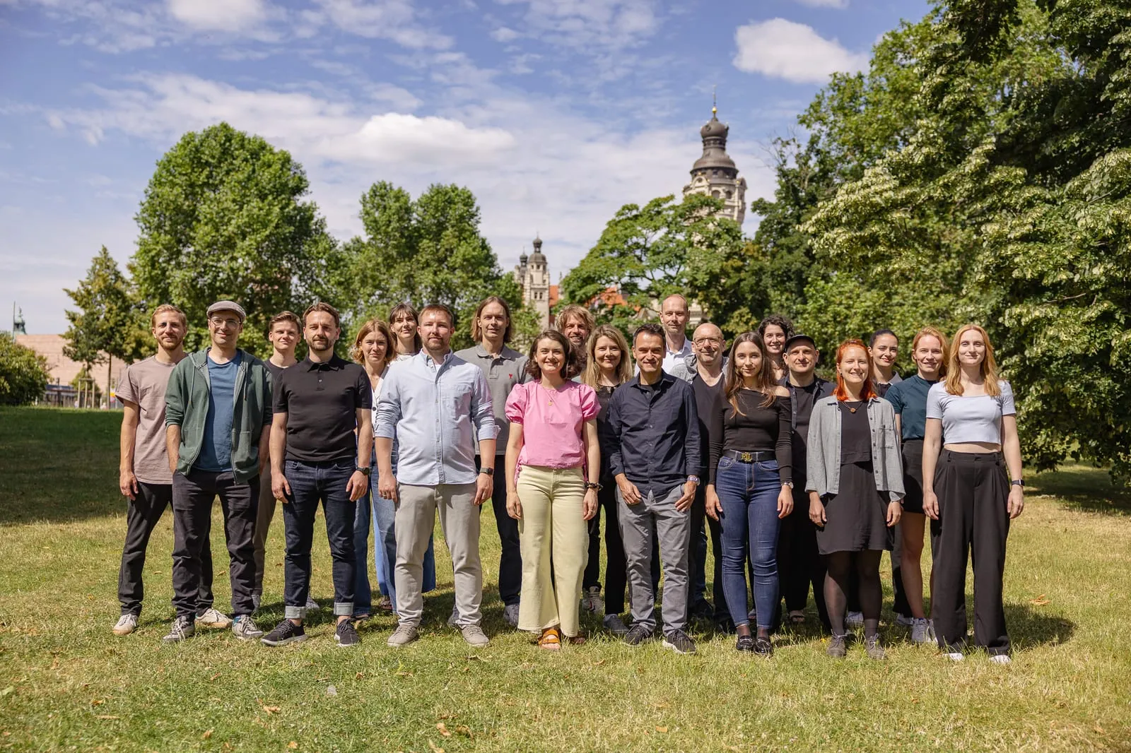 Gruppenfoto von rund 20 Mitarbeitenden auf einer Parkwiese, im Hintergrund Bäume und ein Turm.