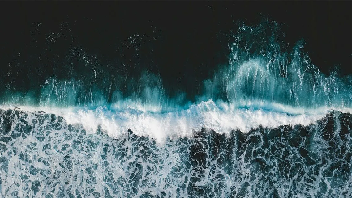 Luftaufnahme einer brechenden Meereswelle mit weißer Gischt auf dunklem Wasser