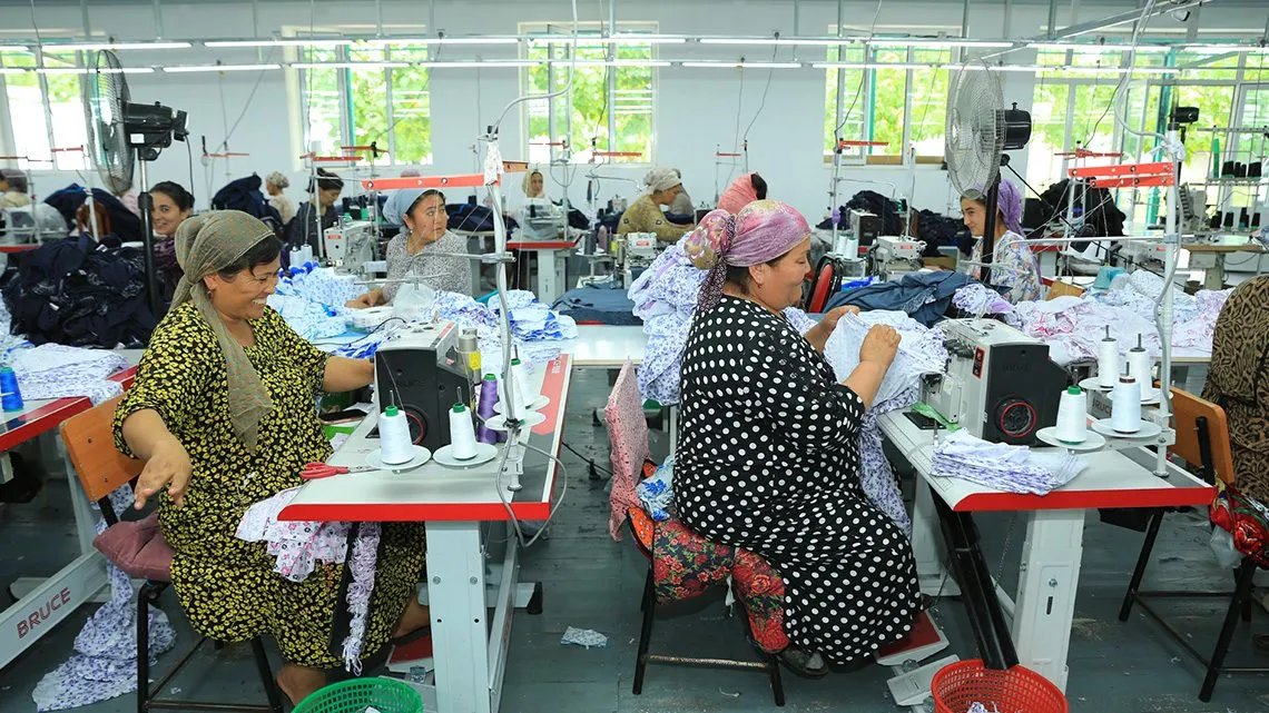 Mehrere Frauen mit Kopftüchern nähen an Industrienähmaschinen in einer hellen Textilfabrik