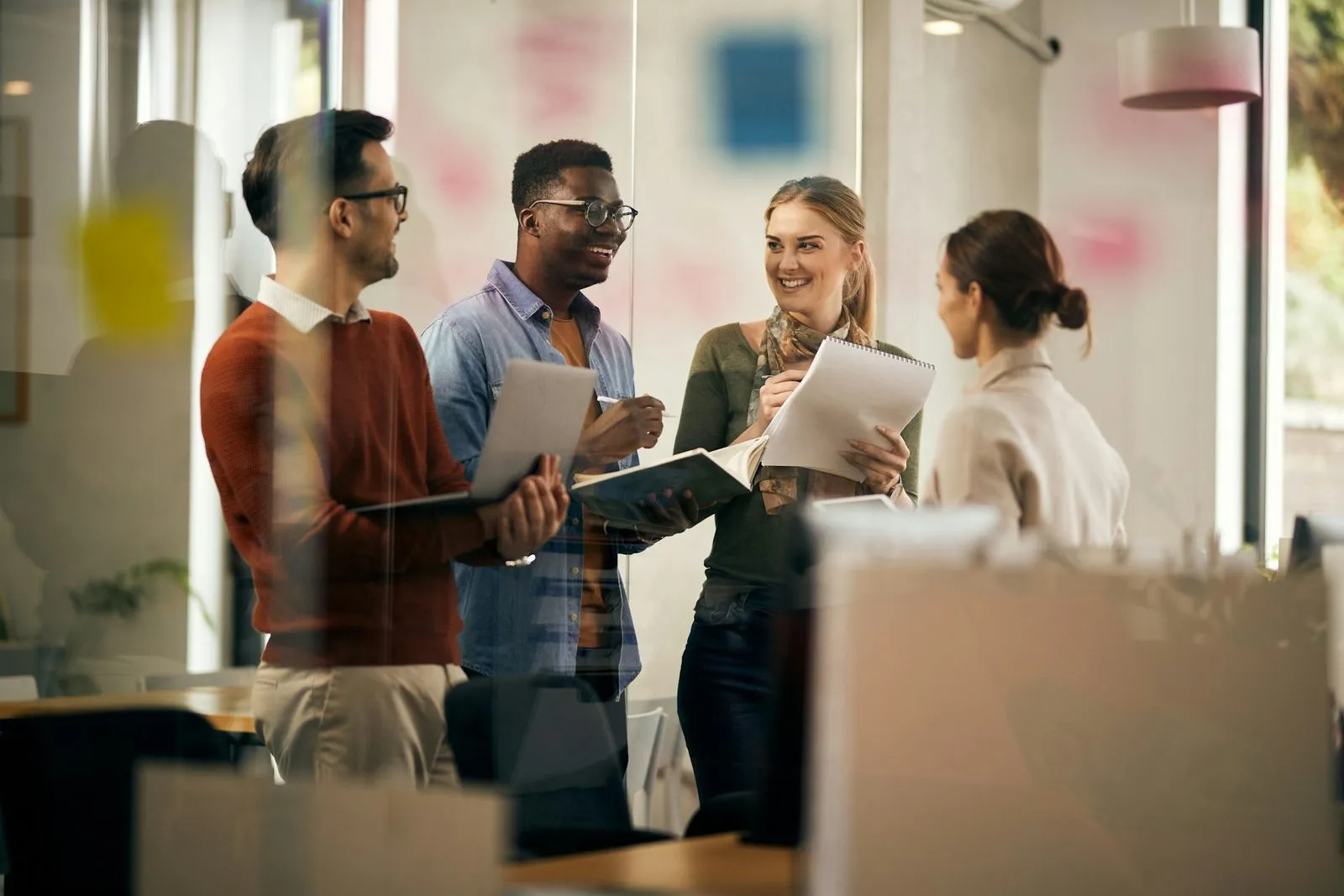 Fröhliches Team spricht stehend miteinander im Büro.