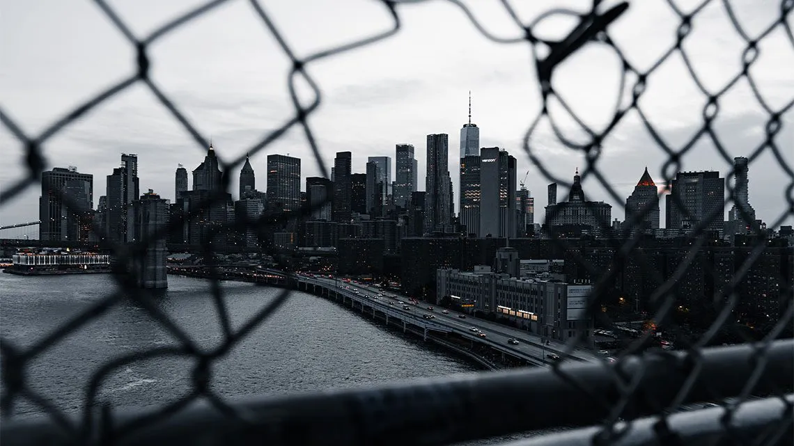 Blick durch einen Maschendrahtzaun auf die Skyline von Manhattan in der Abenddämmerung