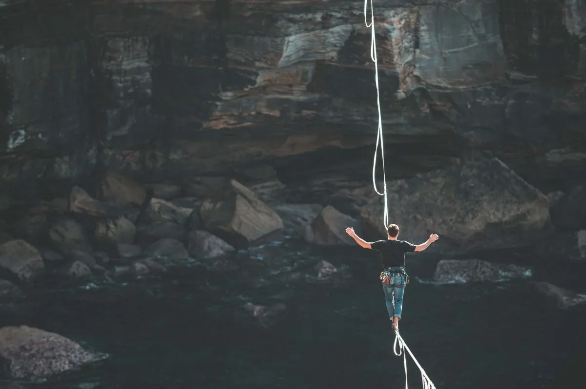 Mann balanciert auf einer Slackline hoch über einer Felsschlucht mit Wasser