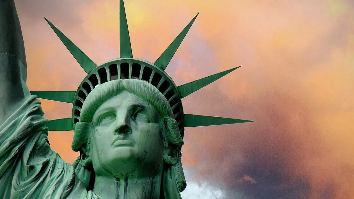Kopf der Freiheitsstatue in Nahaufnahme vor orange-violettem Wolkenhimmel