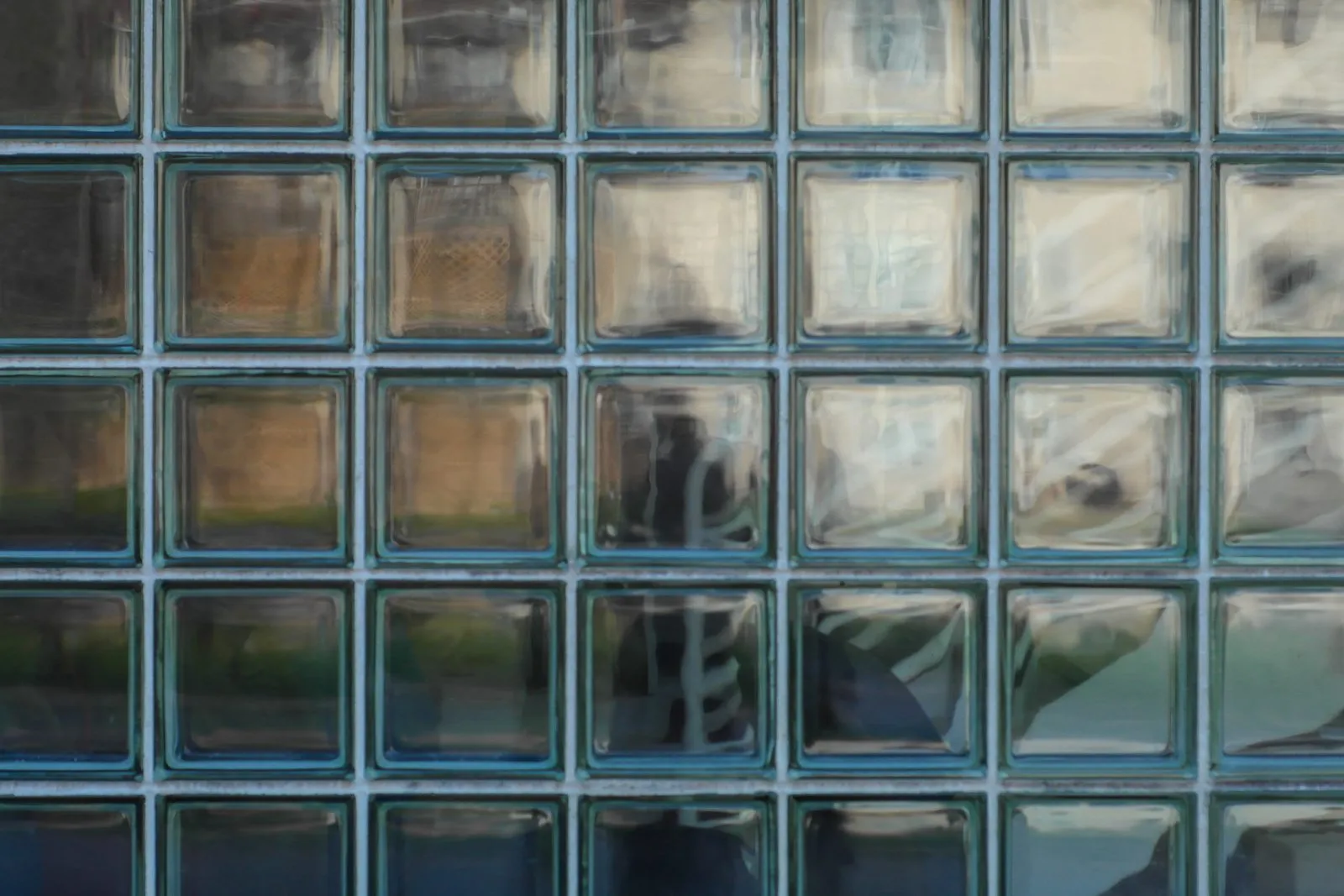 Fassade aus Glasbausteinen mit verschwommenen Reflexionen und Schattenumriss einer Person dahinter