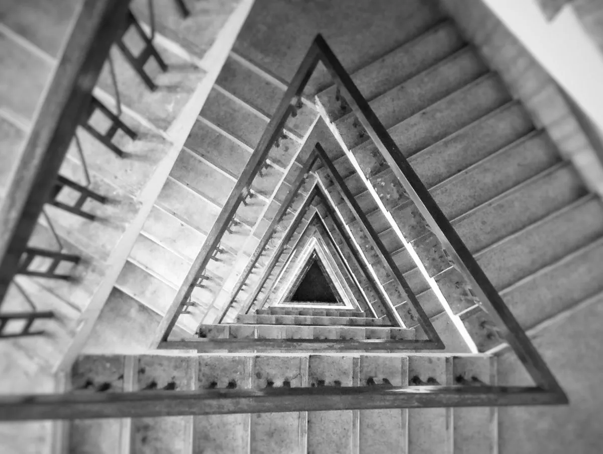 Schwarz-weiß-Aufnahme einer Wendeltreppe von oben, die sich zu einem Dreieck verjüngt